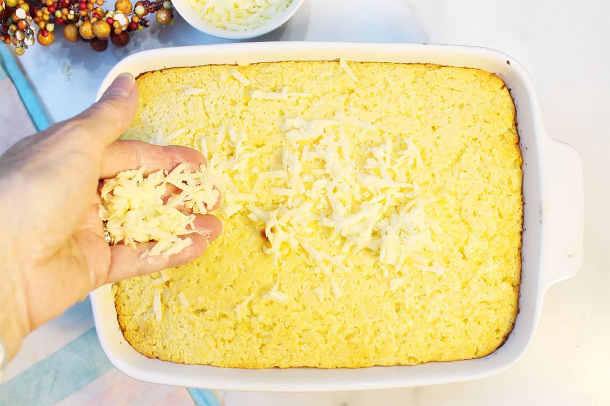 Sprinkling cheese on corn pudding casserole after first bake.