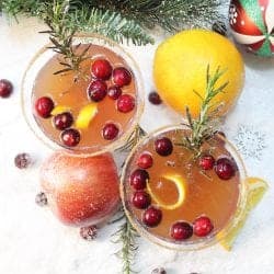 Overhead of cocktails on snow with orange apple and ornament around them.