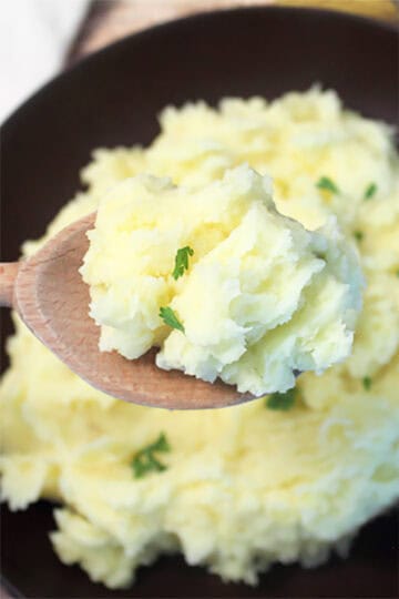 Spoonful of mashed potatoes over bowl.
