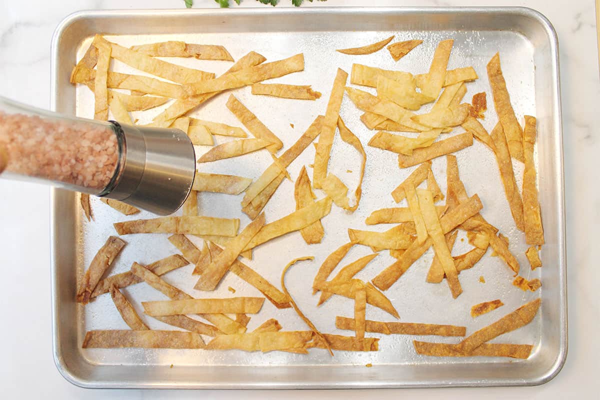 Adding a coating of salt to baked corn chips.