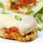 Closeup of plated chicken parmesan showing crispy chicken, layer of sauce and melted cheese.