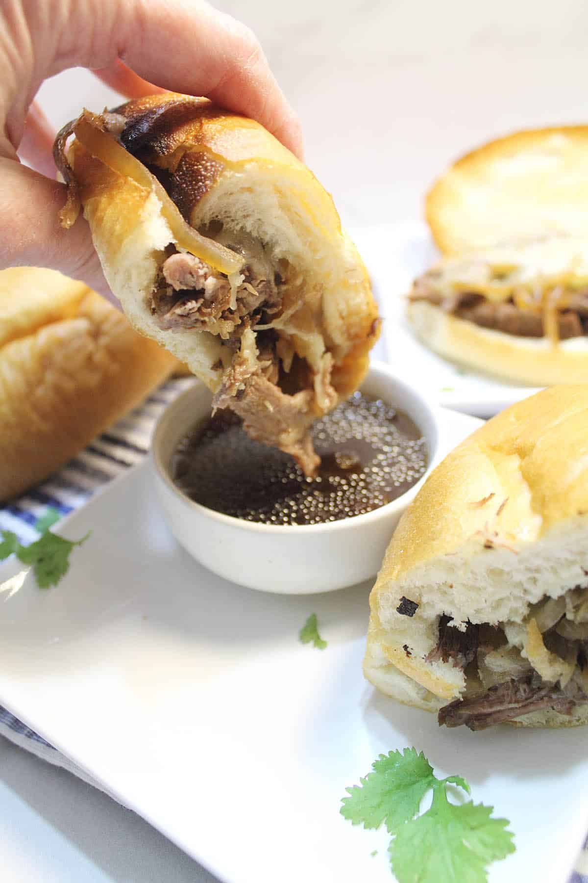 Dipping Crockpot French Dip Sandwich half in au jus.