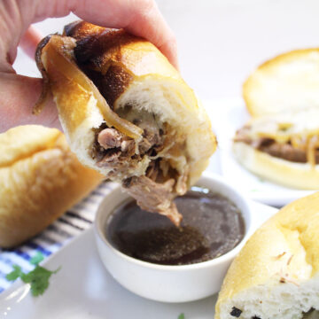 Dipping French dip sandwich into au jus.
