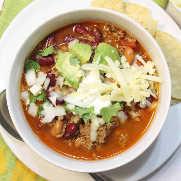 Overhead of white bowl of chili with cheese avocado and sour cream.