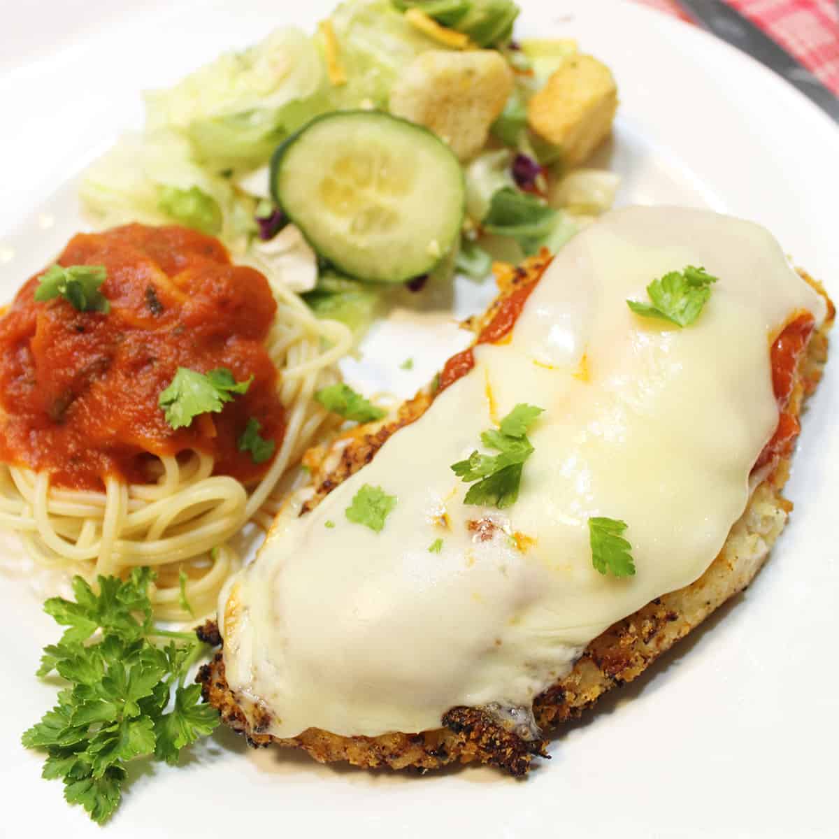 Plated dinner of chicken parmesan with pasta and salad.