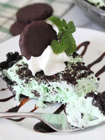 Slice of grasshopper pie on chocolate drizzled plate with fork with bite on it.
