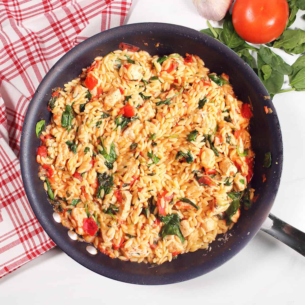 Chicken and Orzo Skillet with tomatoes and red checkered towel.