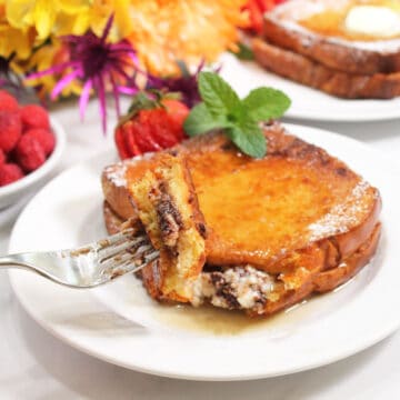 Holding bite of French Toast on fork over plated breakfast.