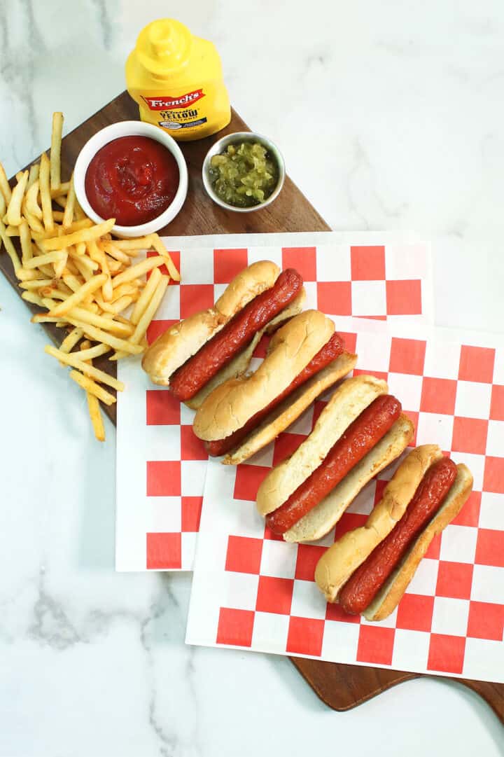 Overhead of hot dogs on wooden board with condiments and french fries.