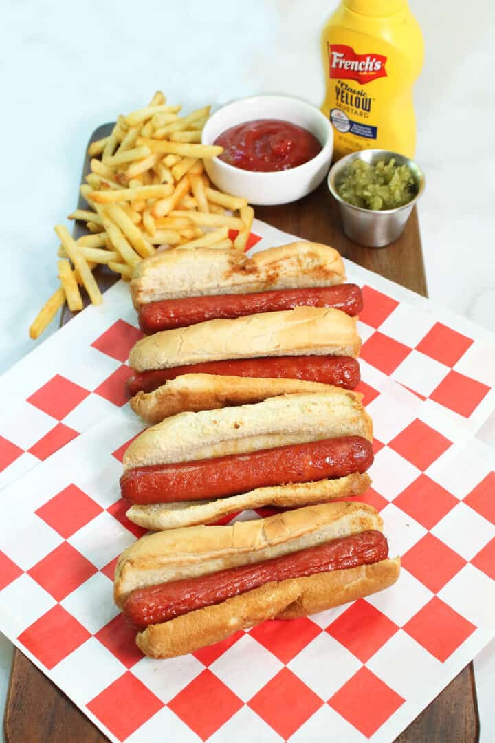 Unadorned hot dogs on red checkered paper with fries and condiments.