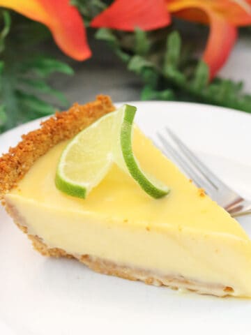 Slice of authentic key lime pie on white plate in front of flowers.