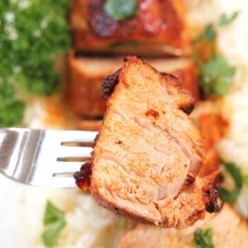 Slice of pork tenderloin on fork over platter.