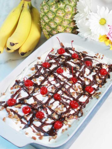 Finished banana split dessert with chocolate drizzle, nuts and cherries.