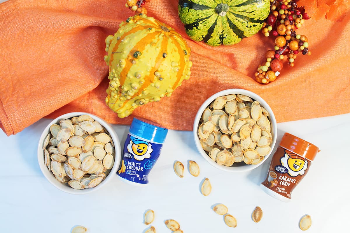 Two bowls of roasted pumpkin seeds with flavorings beside them.