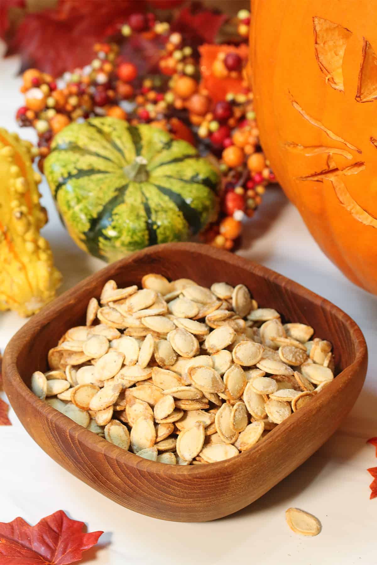 Air fried pumpkin seeds in wooden bowl with colorful gourds in back.