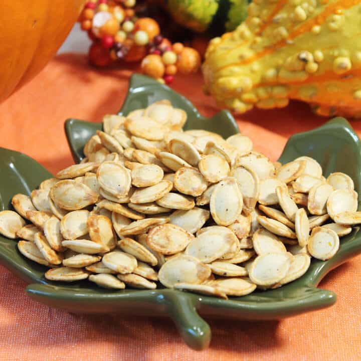 Closeup of pumpkin seeds in green leaf bowl on orange napkin.