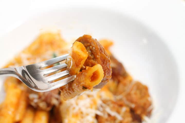 Bite of pasta and sausage covered with pumpkin sauce over serving bowl.