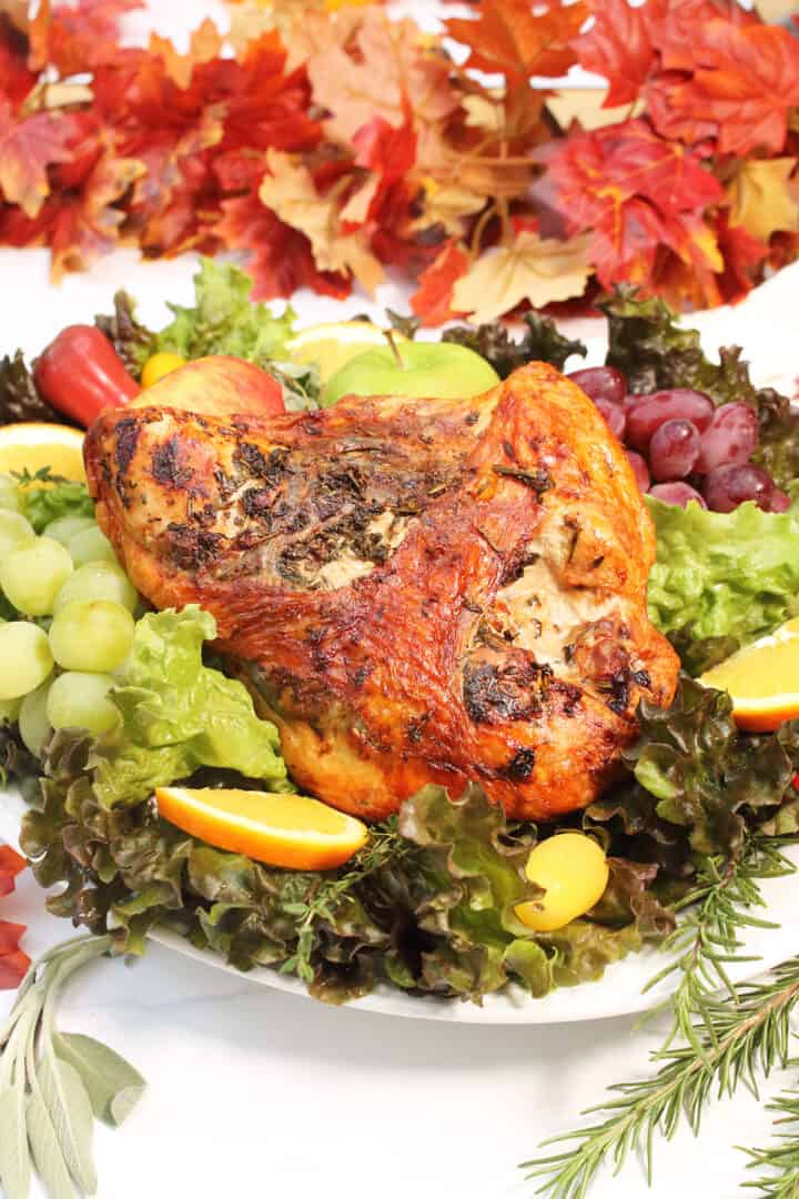 Air Fried turkey breast on platter with fruits and fall leaves in back.