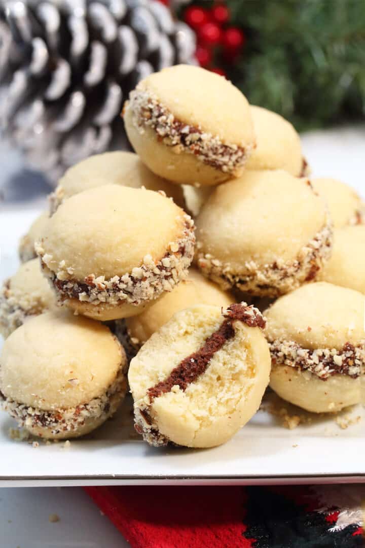 Closeup of shortbread sandwich cookies on white plate with bite taken out of one.