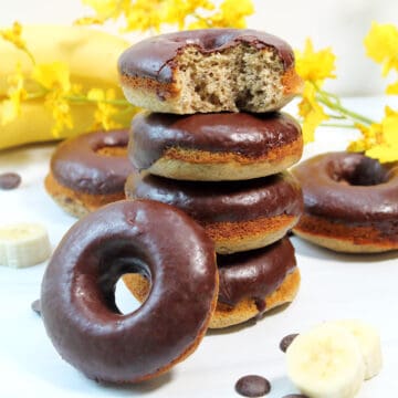 Baked banana donuts with chocolate glaze stacked with one leaning on side.