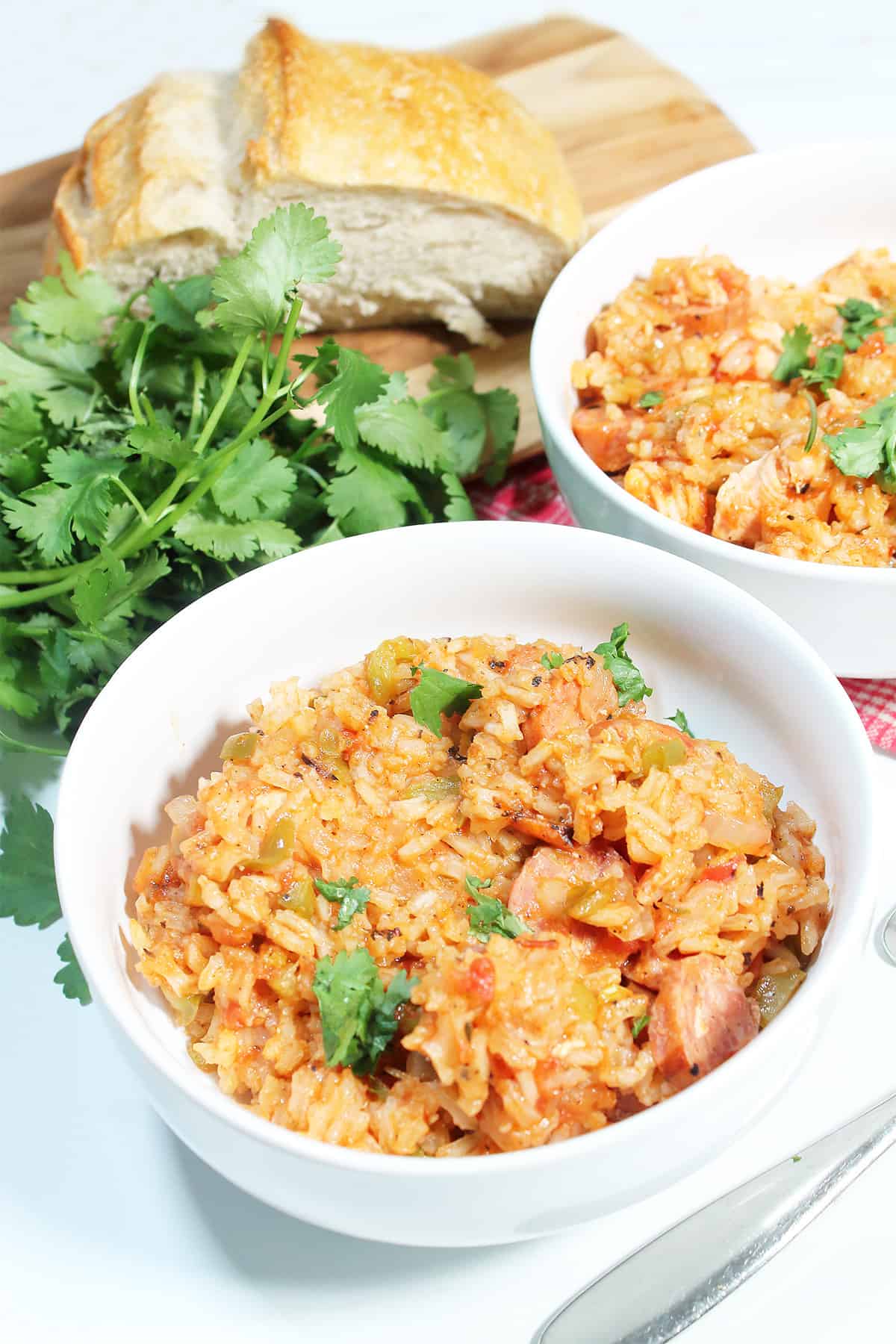 Two bowls of jambalaya with bread and parsley in back.