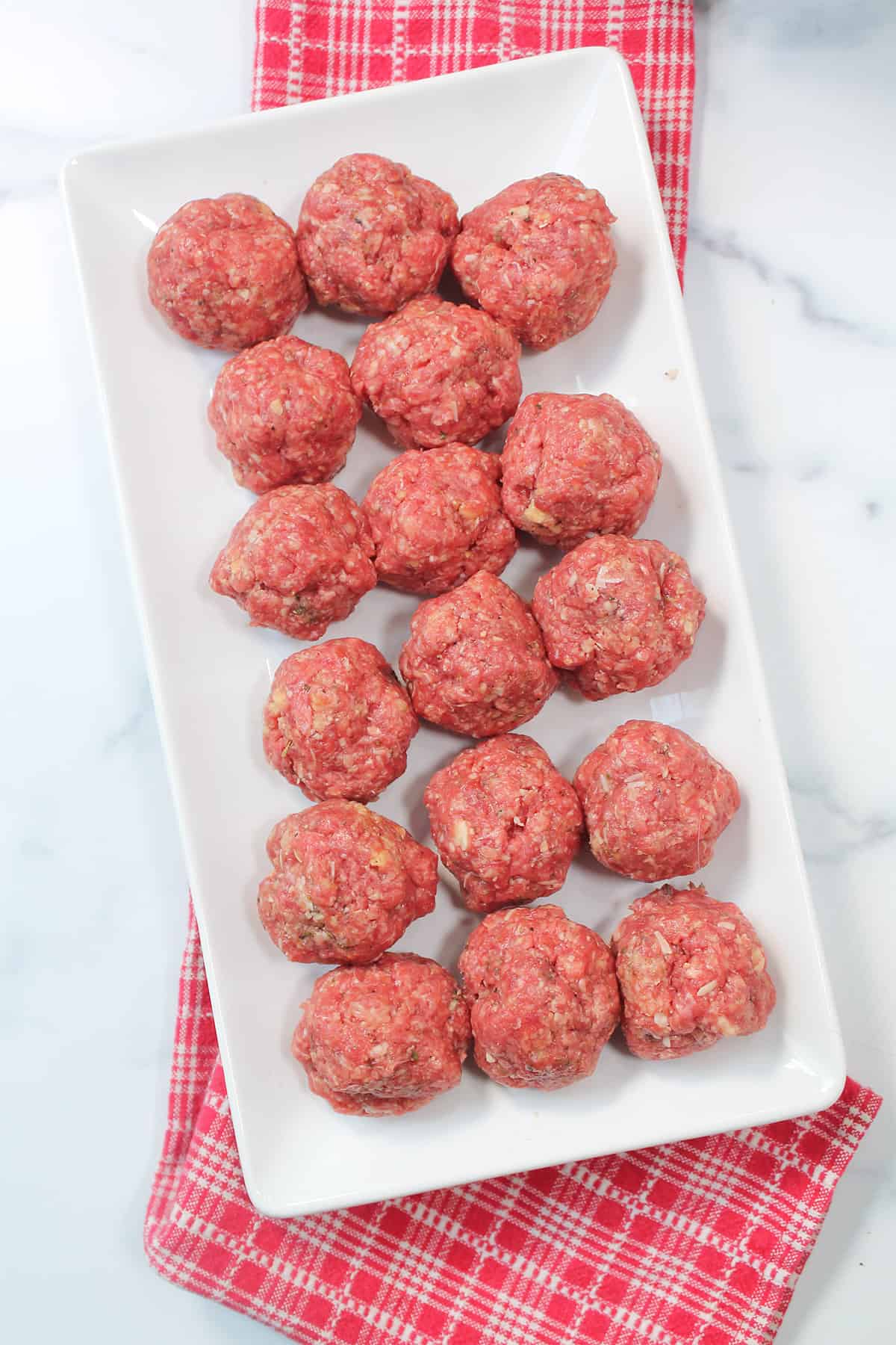 Meatballs laid out on white platter over red checkered towel.