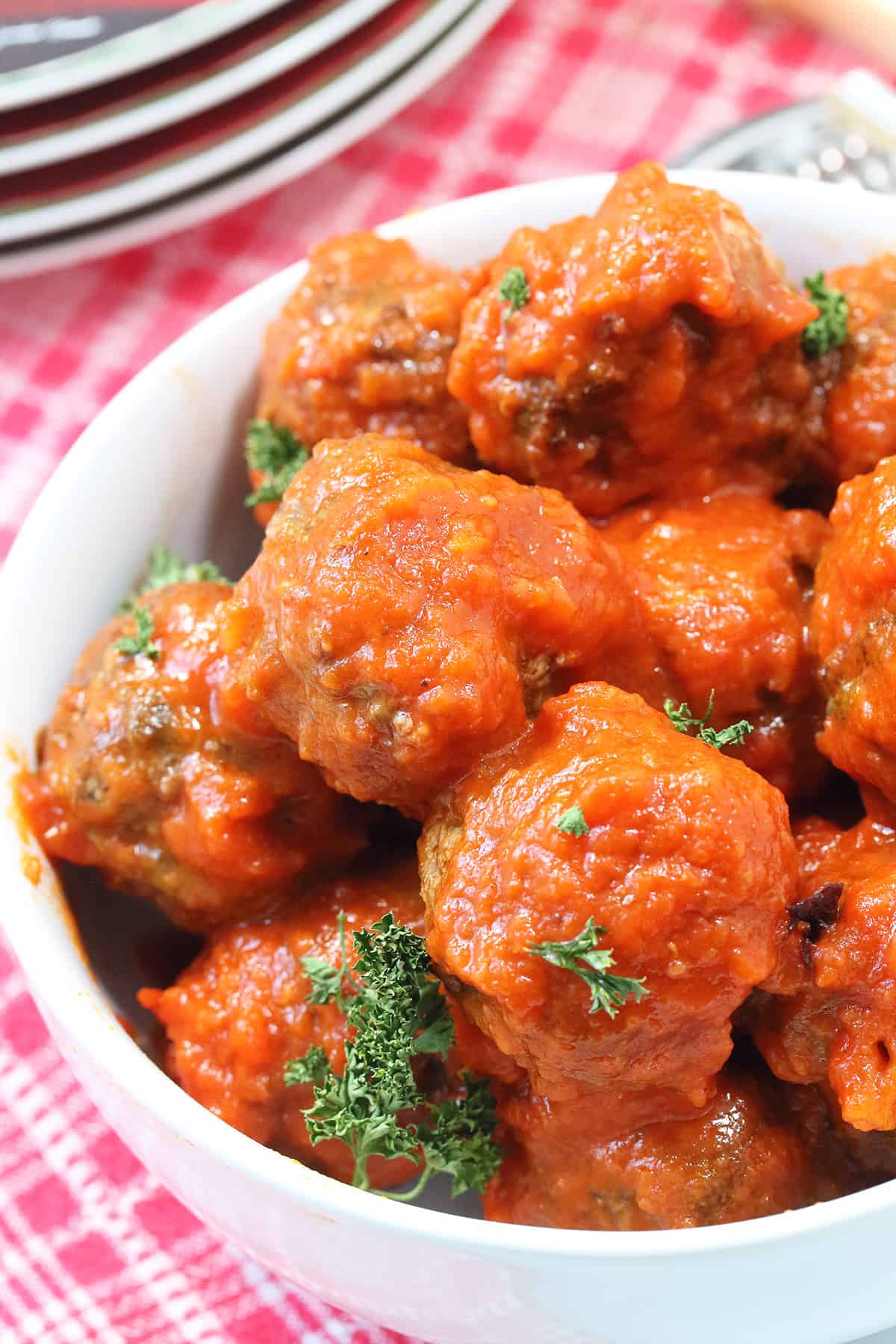 Partial closeup view of air fried meatballs covered in sauce in white bowl.