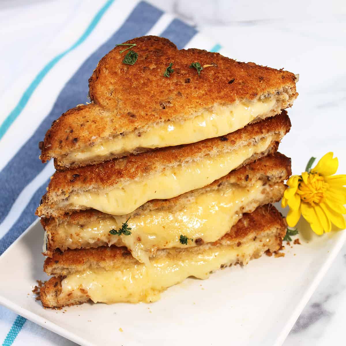 Stacked air fryer grilled cheese on white plate with striped towel.