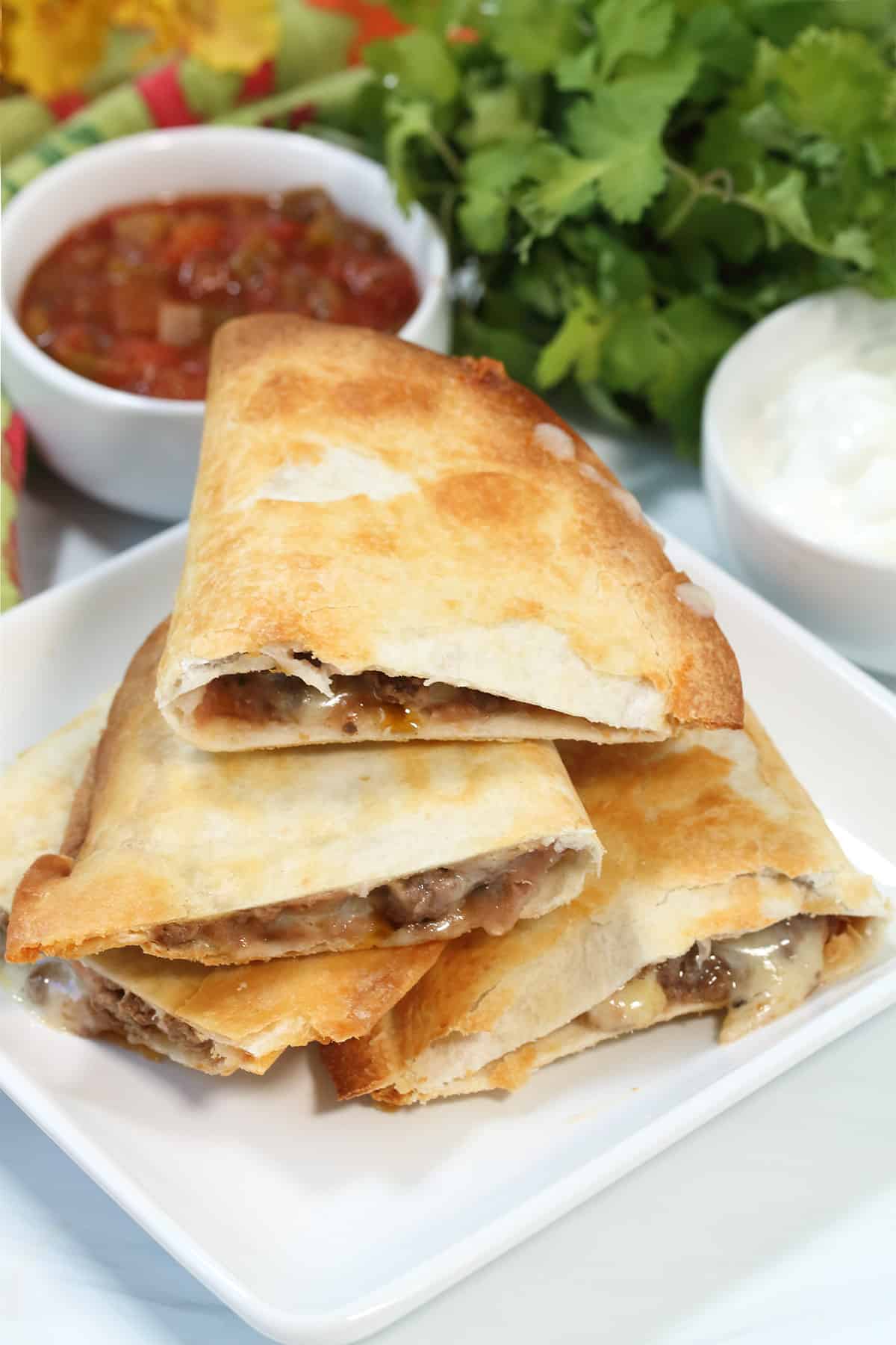 Quesadillas stacked on white plate with salsa and cilantro in back.
