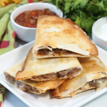 Crispy quesadillas cut in half and piled on plate with salsa in back.