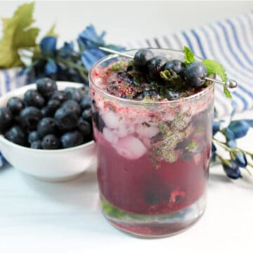 Mojito with blueberries and mint next to bowl of blueberries.