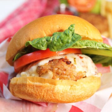 Holding air fryer turkey burger on bun with lettuce, tomato and cheese.