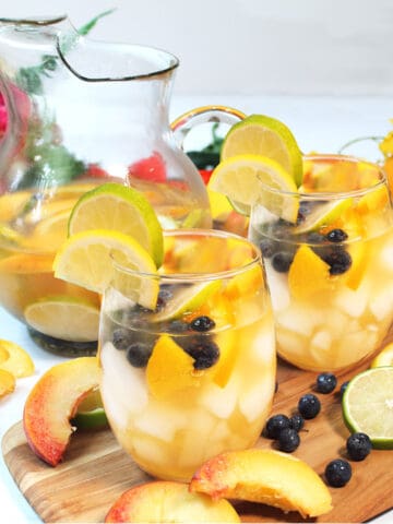 Glasses filled with fruit and sangria on wooden board.
