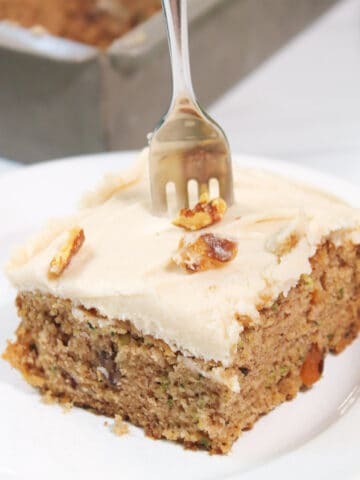 Slice of zucchini cake with cream cheese frosting with fork in it.