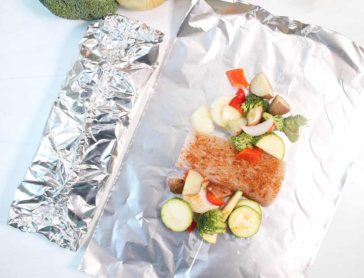 Placing fish and vegetables in foil and wrapping up securely.