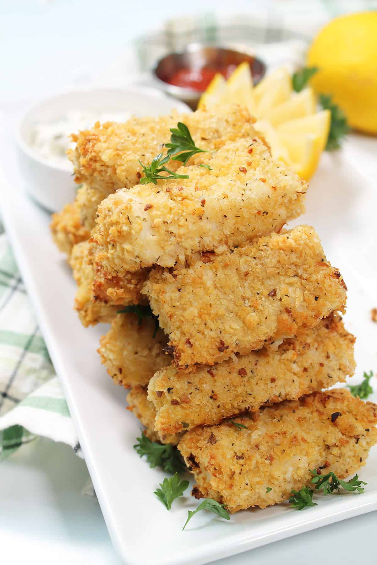 Stacked Air Fryer Fish Sticks on platter with tartar sauce, lemon wedge and cocktail sauce.