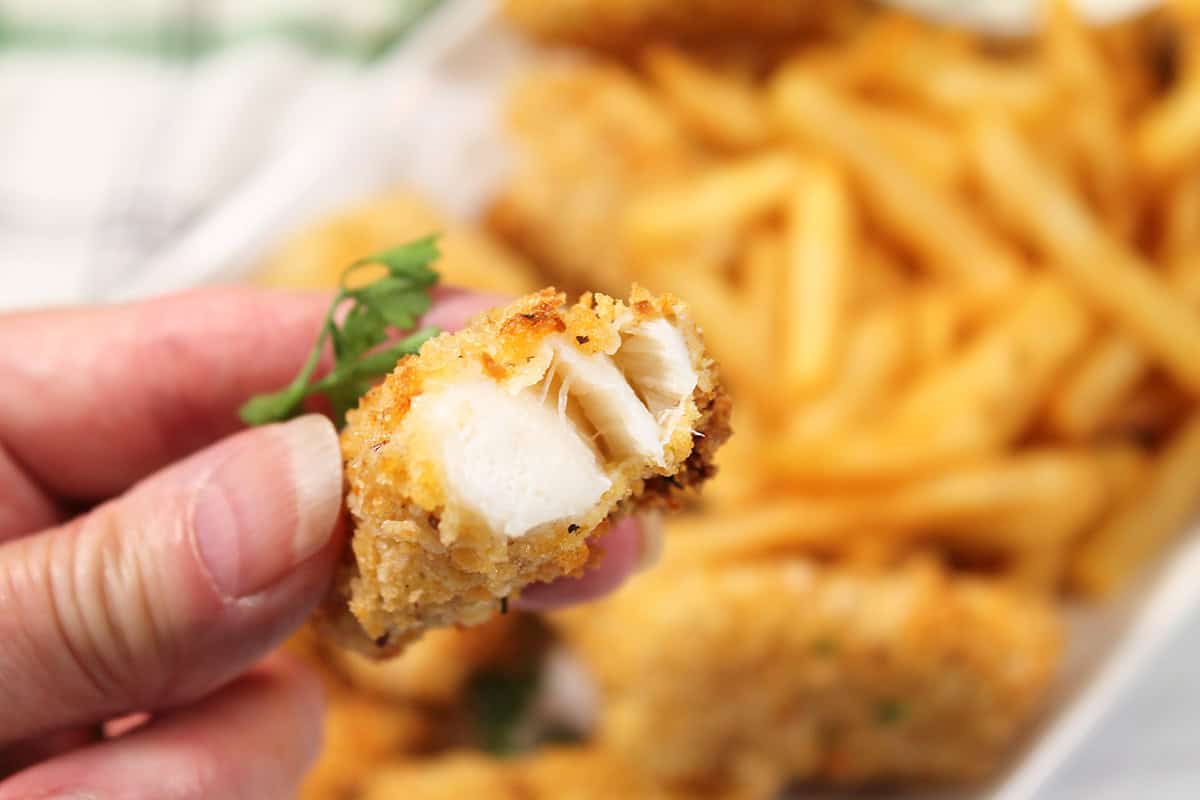 Holding air fried fish stick with bite out.