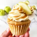 Holding cupcake with frosting and apple garnish.