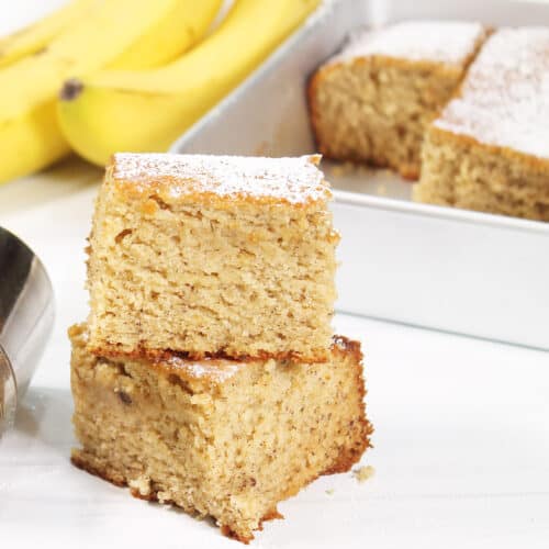 Two pieces of Banana Snack Cake stacked in front of pan.