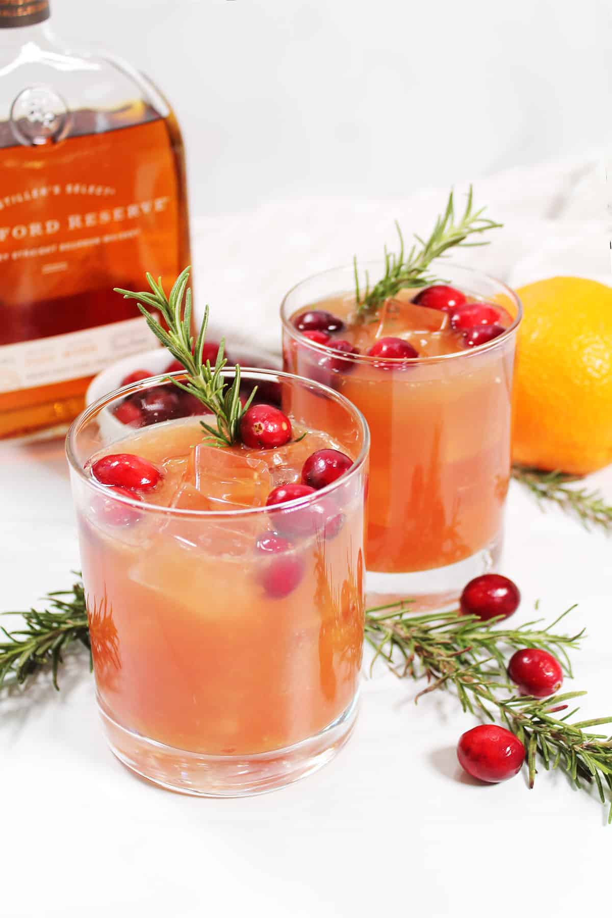 Two glasses of cranberry bourbon cocktail with cranberries and orange.
