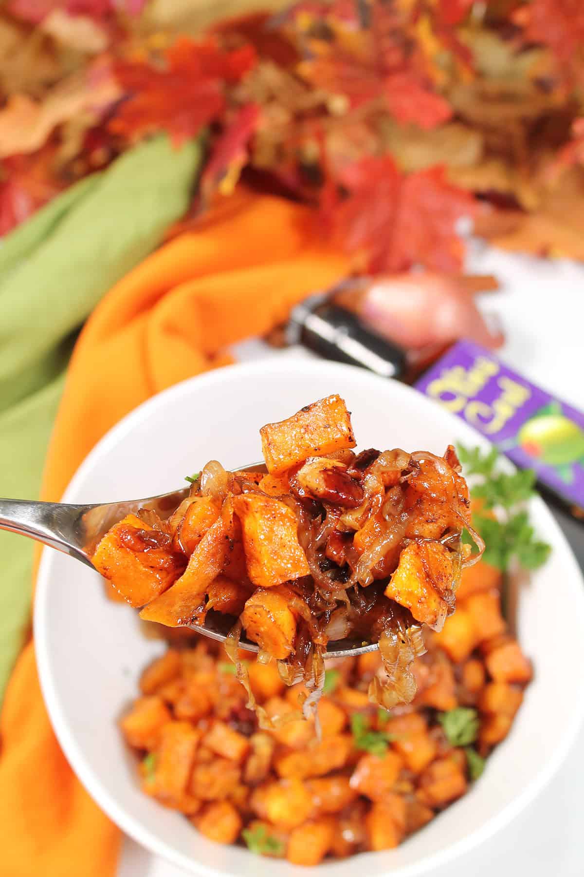 Spoonful of Maple Roasted Sweet Potatoes over bowl with parsley garnish.