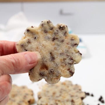 Holding Toffee Chocolate Chip Shortbread Cookie over table.