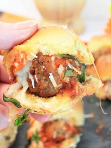 Holding meatball slider above tray of sliders.