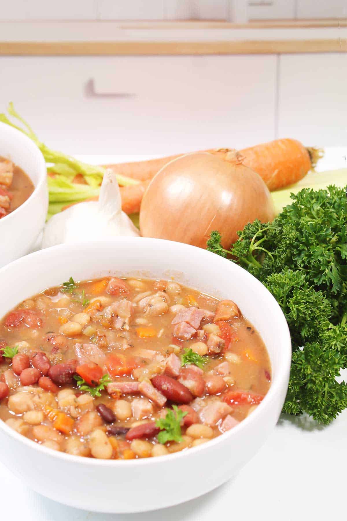 15 Bean Soup with Ham in bowl with fresh vegetables.