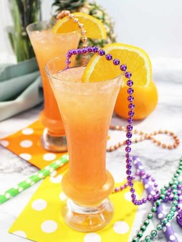 Hurricane cocktail with orange garnish among beads.