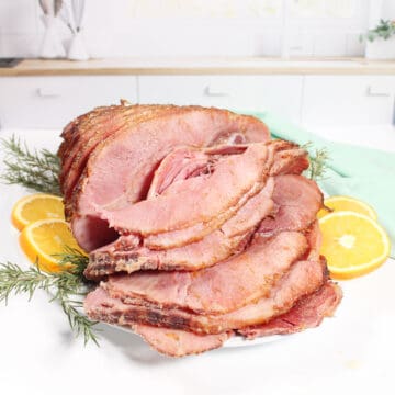 Sliced maple brown sugar glazed ham on platter with orange slices.