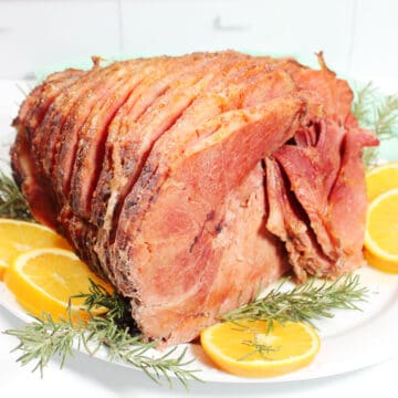 Ham on platter with orange slices and rosemary.
