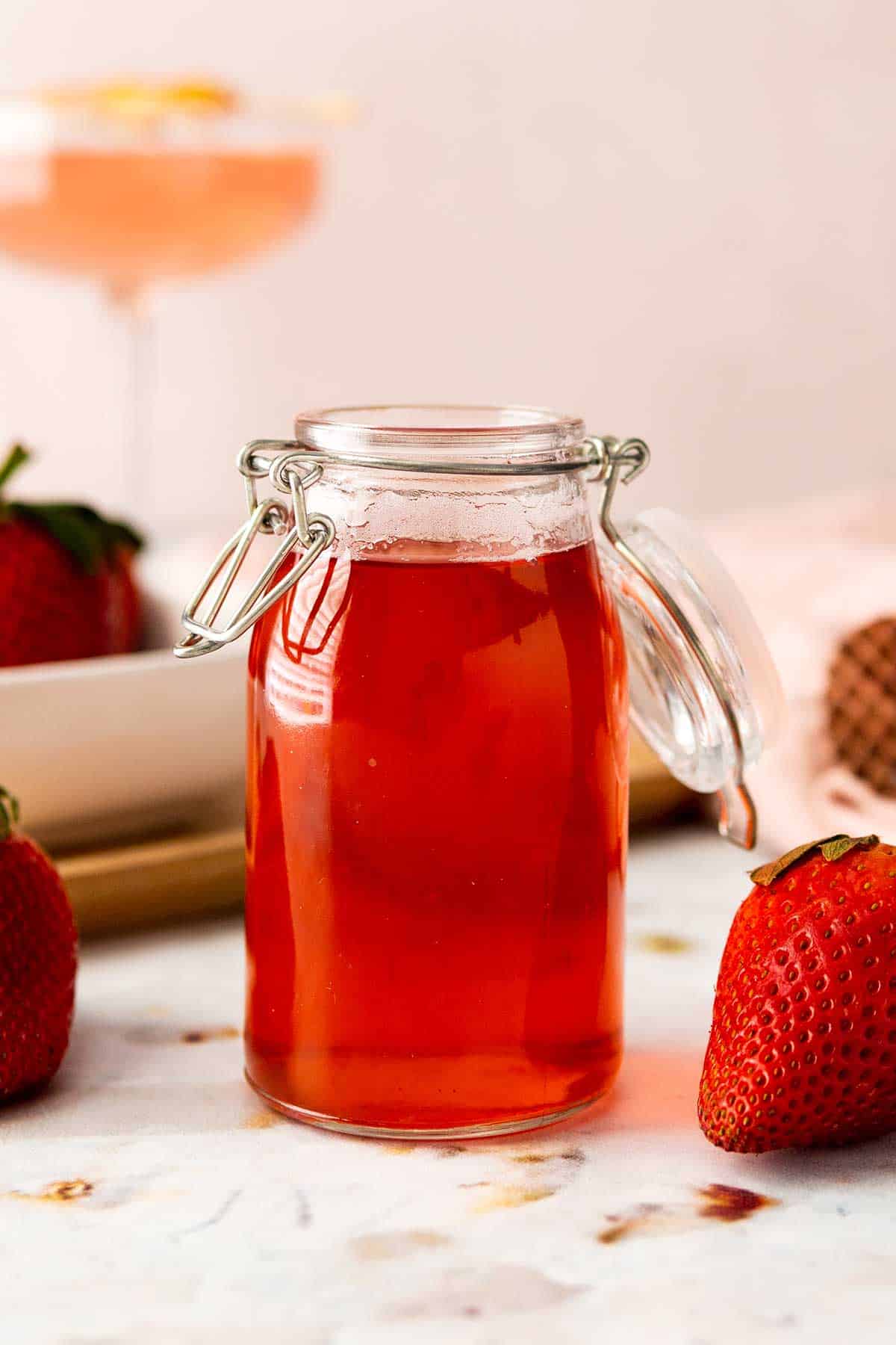 Closeup of strawberry simple syrup with martini in back.