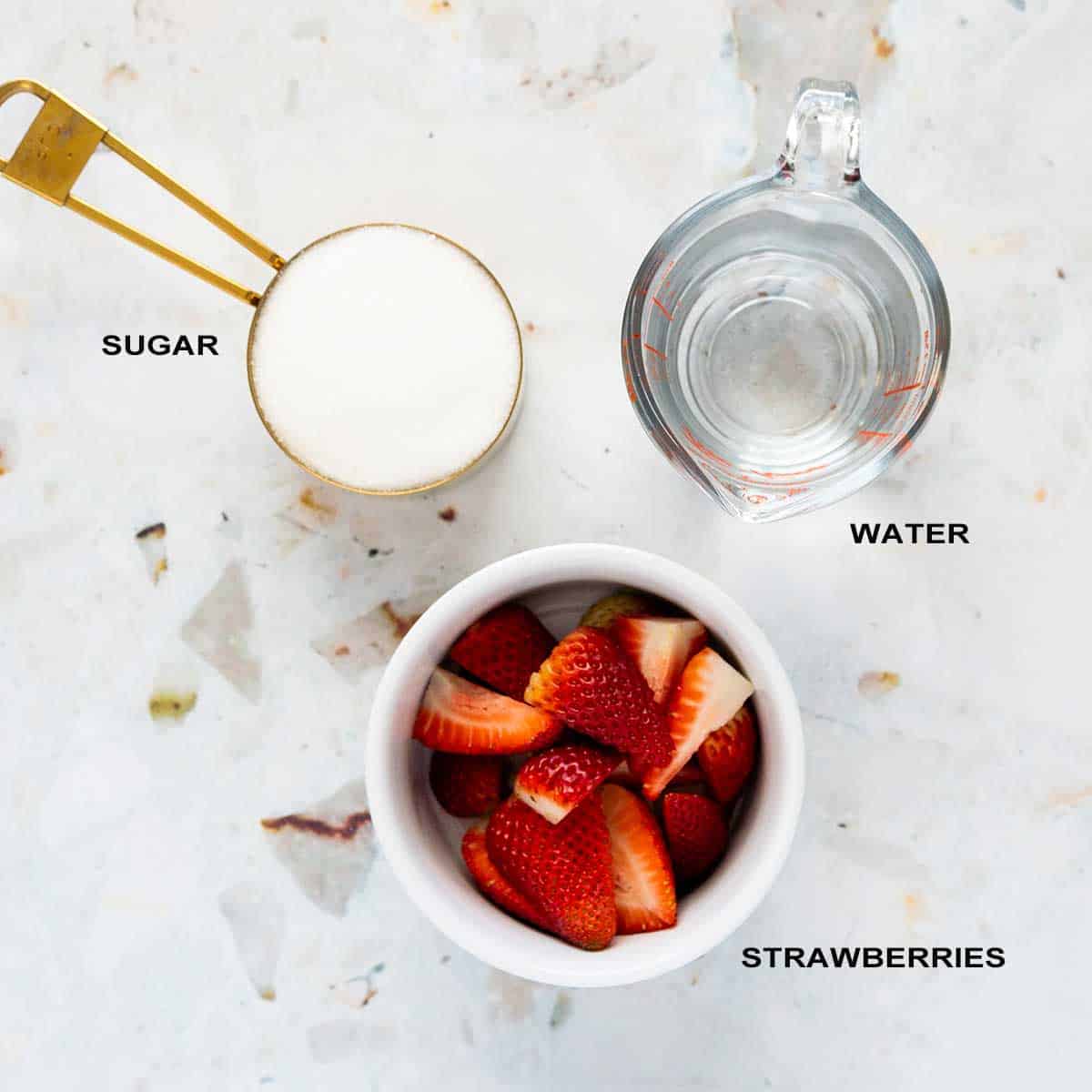 Ingredients for strawberry syrup on white counter.