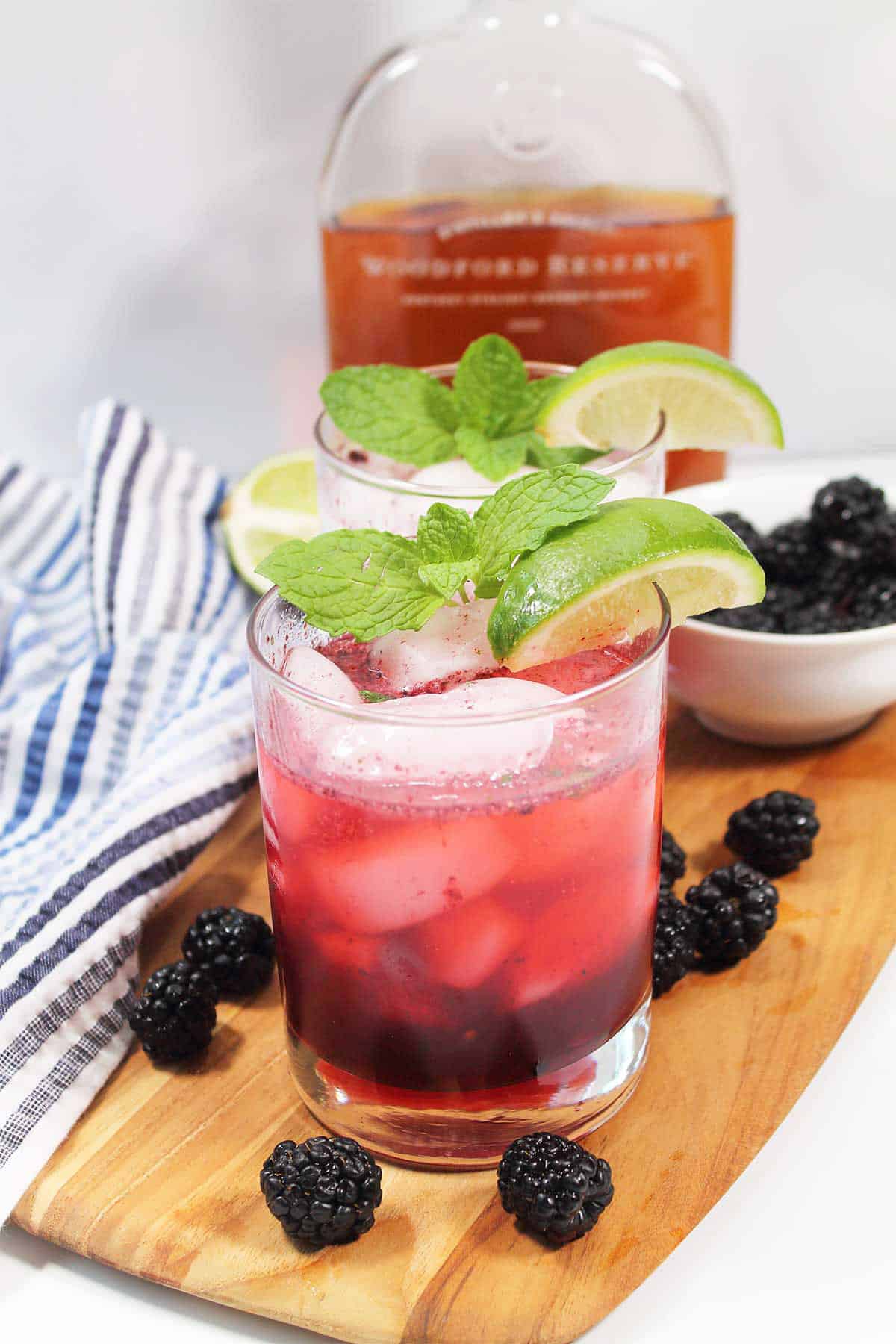 Two blackberry bourbon smash cocktails with mint and lime garnish.